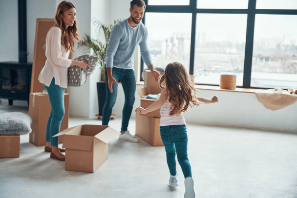 Playful young family smiling and unboxing their stuff while moving into a new apartment - Fotó, kép