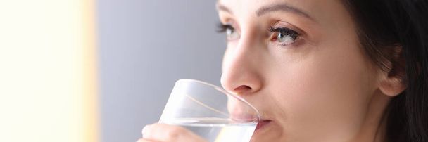 Egy fiatal nő poharat tart a kezében és vizet iszik belőle. - Fotó, kép