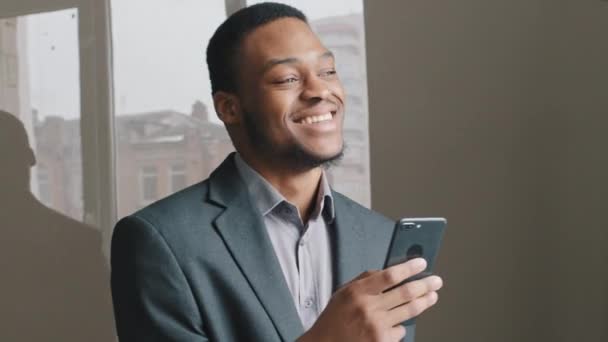 Homem negro animado trabalhando em aplicativo digital segurar smartphone ler boas notícias da internet, cara africano feliz olhar para a tela do telefone alegrou-se com o sucesso da vitória. Millennial empresário usuário de tecnologia móvel - Filmagem, Vídeo