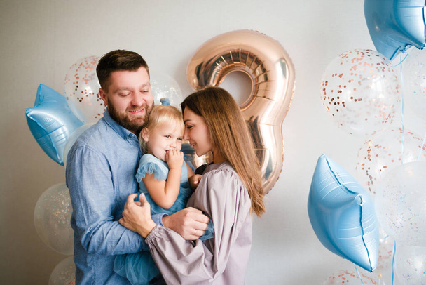Family celebrates the birthday of their little daughter. Birthday celebration in blue dresses and balloons.  - Zdjęcie, obraz