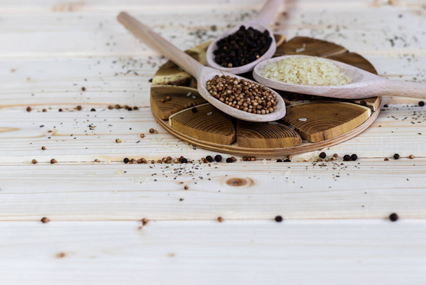 Three wooden spoons with spices, coriander, peppercorns and rice on a wooden background. Rustic look and copy space - Photo, Image