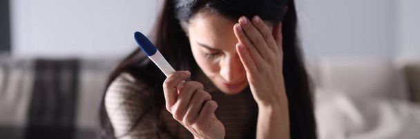 Sad woman sitting on couch and holding pregnancy test closeup - Photo, Image