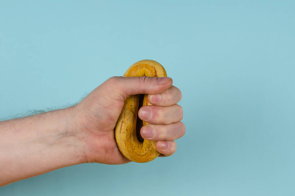 Die Hand umklammert ein gelbes Gummiband auf blauem Hintergrund. Erwachsene Männer halten einen runden Handtrainer in der Hand. Seitenansicht. Sport, aktiver Lebensstil. - Foto, Bild