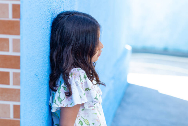 A girl, child, Brazilian, with a serene expression, straight black hair and leaning against the wall. - Fotó, kép