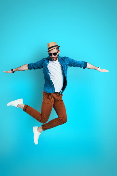Full length of handsome young man keeping arms outstretched while hovering against blue background - 写真・画像