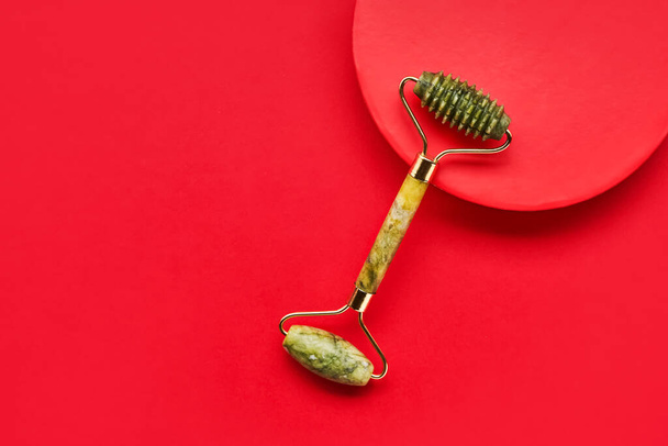 Green face roller from natural jade stone on a bright red background. SPA concept. Top view, copy space for text - Photo, Image
