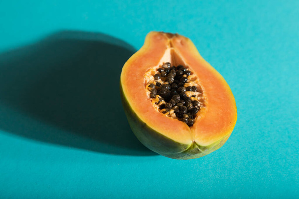 Kypsä leikattu papaija sinisellä pastellitaustalla. Sivukuva, lähikuva, kova valo. Trooppinen, terveellinen ruoka, naisten terveyden käsite, minimalismi. - Valokuva, kuva