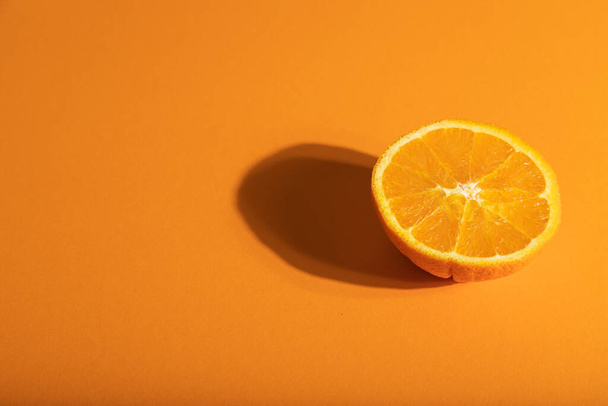Dojrzała pomarańcza na pomarańczowym pastelowym tle. Widok z boku, przestrzeń do kopiowania, twarde światło. Tropikalna, zdrowa koncepcja żywności, minimalizm. - Zdjęcie, obraz