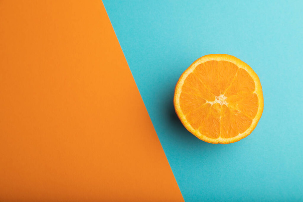 Ώριμο κομμένο πορτοκάλι σε πορτοκαλί και μπλε παστέλ φόντο. Πάνω άποψη, επίπεδη lay, αντίγραφο χώρου. Τροπικά, υγιεινά τρόφιμα, έννοια, μινιμαλισμός. - Φωτογραφία, εικόνα