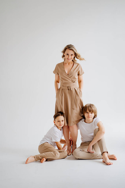 A mother and her two sons in beige and white clothes pose for a photo shoot  - 写真・画像