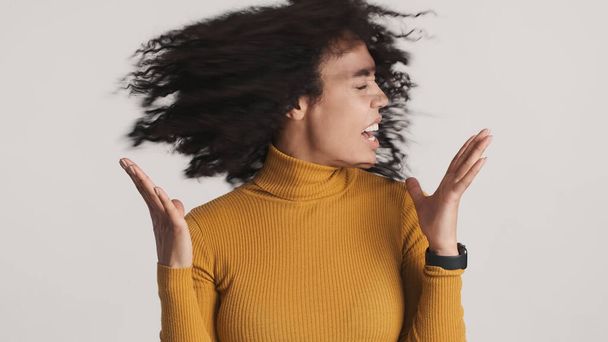 Emotional African American woman with dark fluffy hair waving head on camera over white background - Photo, Image