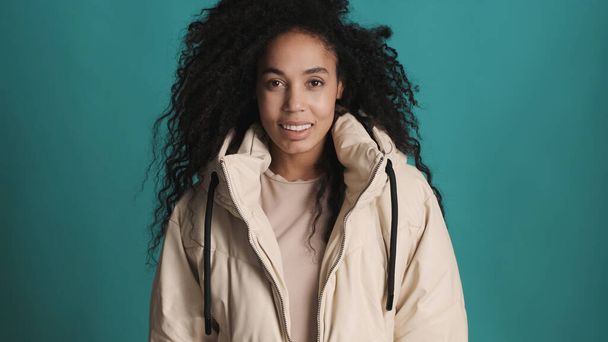 Young pretty Afro woman dressed in down jacket looking happy  smiling on camera over colorful background - Photo, Image