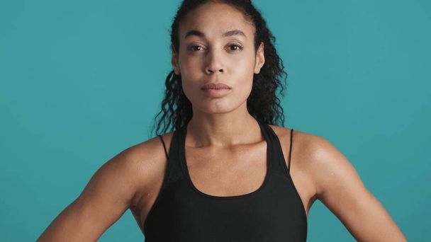 Young beautiful African American woman dressed in sport bra looking confident after workout over blue background. Sporty girl - Foto, Imagen