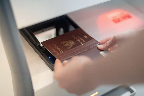 Женщина, держащая в руках личный паспорт, сканирует его в кассе самообслуживания для получения посадочного талона в терминале аэропорта. - Фото, изображение