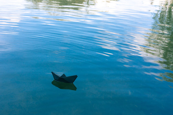 Black paper boat floats on the river - 写真・画像