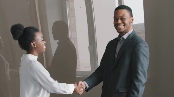 Счастливая молодая афроамериканская этническая предпринимательница пожимает руку работодателю-мужчине после переговоров по проекту, успешной деловой встречи, заключения сделки в офисе. Стажеры получают положительные отзывы. - Кадры, видео