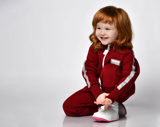 Little preschooler girl wearing warm tracksuit sitting on studio floor - Foto, Imagen