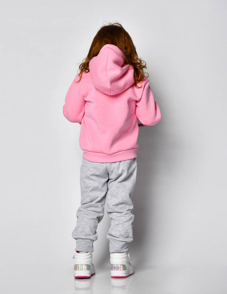 Rear view of a redhead girl in a pink sweatshirt walking towards the free copy space against a gray wall. - Фото, зображення