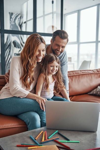 Young beautiful family with little girl bonding together and smiling while using laptop at home - Fotoğraf, Görsel