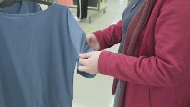 Valkoihoinen raskaana oleva nainen valitsee sininen pusero varastossa ostaa. Kädet lähemmäs. - Materiaali, video
