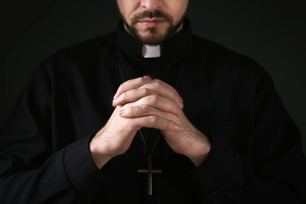 Priest in cassock praying on dark background, closeup - Фото, зображення
