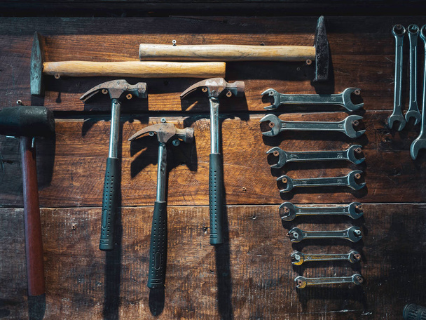 Set of wrench and old hammers hanging on wooden wall background, vertical style. Many size of wrenches and hammers on wood plank wall. - 写真・画像