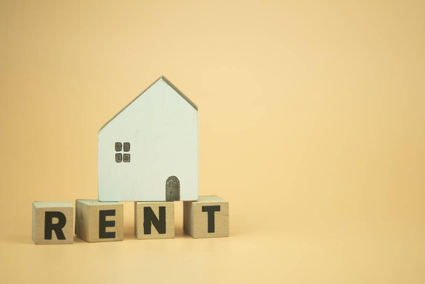 黄色の背景の上に木製の家で文字RENTと木製のブロック。賃貸住宅のコンセプト - 写真・画像
