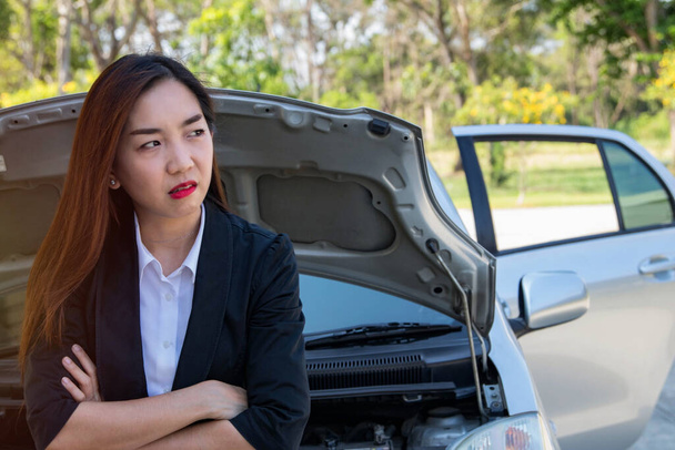 Businesswoman standing in front of her saloon, opened the hood, made her face tense, scratching her head, frustrated, because of the problem of getting lost and damaged cars at the same time ,  - Photo, Image