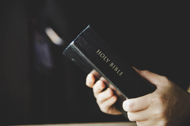 Woman holding the bible in hands on black with copy space. - Foto, afbeelding
