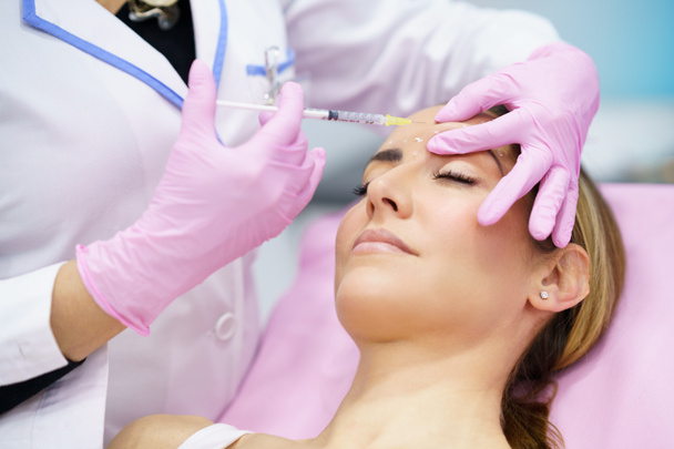 Esthetische arts die botox injecteert in het voorhoofd van haar patiënt van middelbare leeftijd. - Foto, afbeelding
