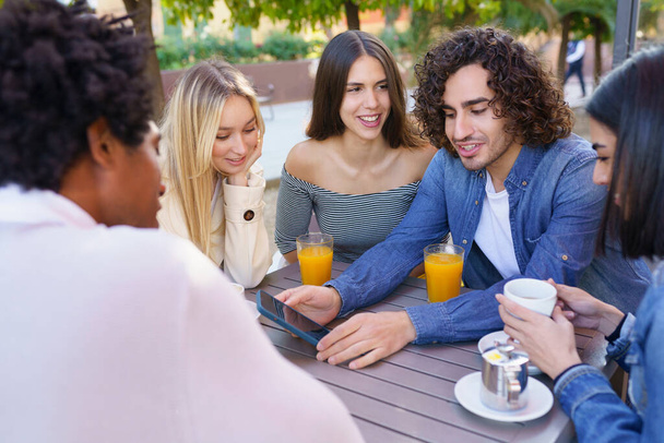 Le gars montre son smartphone à son groupe d'amis en buvant un verre dans un bar extérieur - Photo, image
