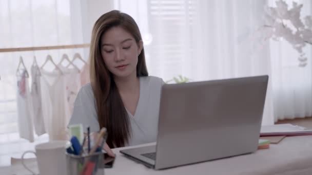 Деловая азиатская женщина разговаривает по телефону и делает заметки на ноутбуке с работой из дома. - Кадры, видео