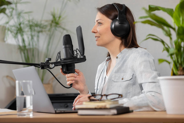 the stylish and educated caucasian woman records podcasts in a recording studio or in her home. the European millennial woman creates audio content or records text, records an audio book or radio show - 写真・画像