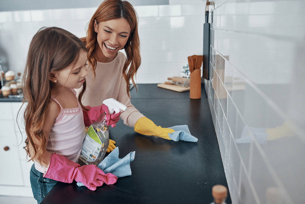 Mother and daughter dusting using washing up gloves while spending time at home - Фото, зображення