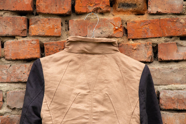 коричнева жіноча куртка, що висить на вішалках на цегляній старій стіні вдома на вулиці, жіноча мода
 - Фото, зображення