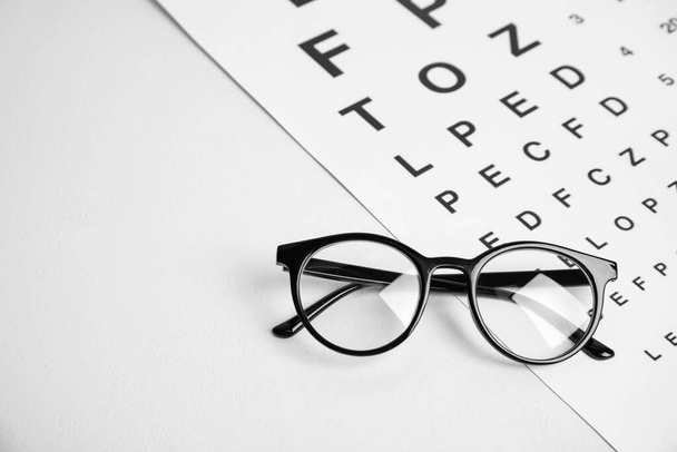 Glasses and eye chart test on white table, space for text. Ophthalmologist tools - Φωτογραφία, εικόνα