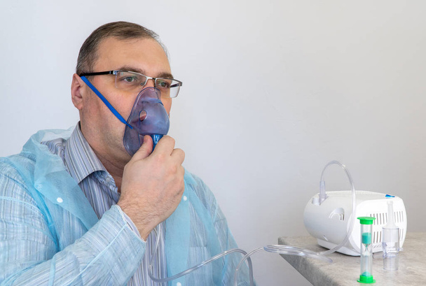 pessoa adulta faz inalações com a ajuda de nebulizador. paciente respira através de uma máscara de oxigênio. o homem está sendo tratado para doenças respiratórias. prevenção da asma - Foto, Imagem