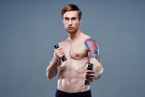 γυμνός άνθρωπος κάνει σπορ σε γκρι φόντο και dumbbell τατουάζ περικοπή άποψη - Φωτογραφία, εικόνα