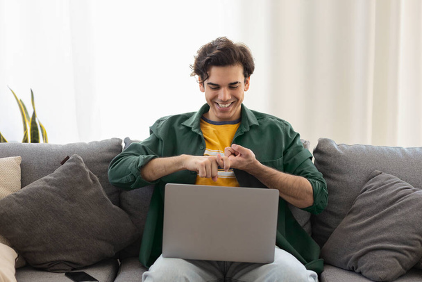 Deaf or hard hearing happy smiling young caucasian man uses sign language while video call using laptop while sitting on the couch at home - Zdjęcie, obraz