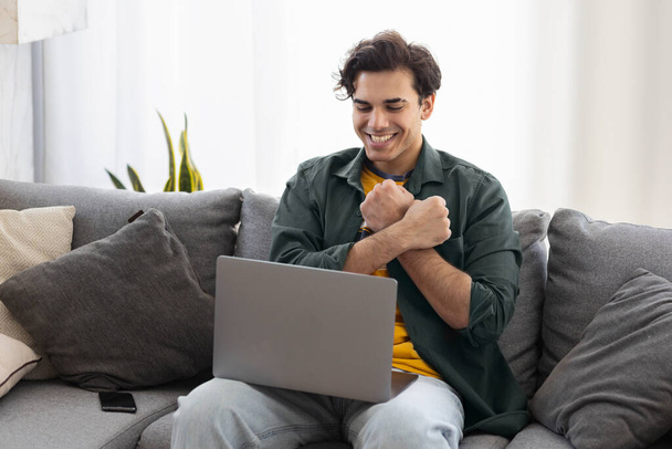 Deaf or hard hearing happy smiling young caucasian man uses sign language while video call using laptop while sitting on the couch at home - Foto, Imagen