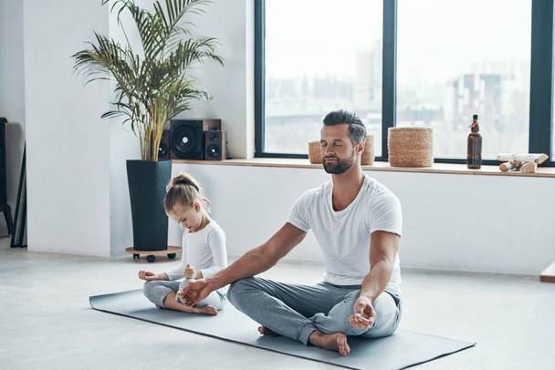 Father and daughter doing yoga while sitting in lotus position at home - Foto, Imagen