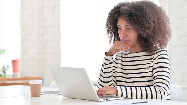 Mujer africana con computadora portátil sentada y pensando  - Foto, imagen
