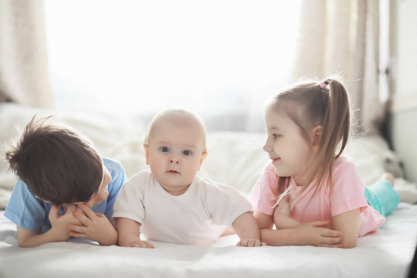 Los niños yacen en la cama junto al bebé recién nacido, hermanita. Emociones infantiles. - Foto, imagen