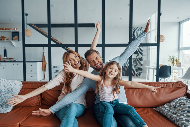 Playful young family stretching out their hands and looking at camera while bonding together at home - Фото, изображение