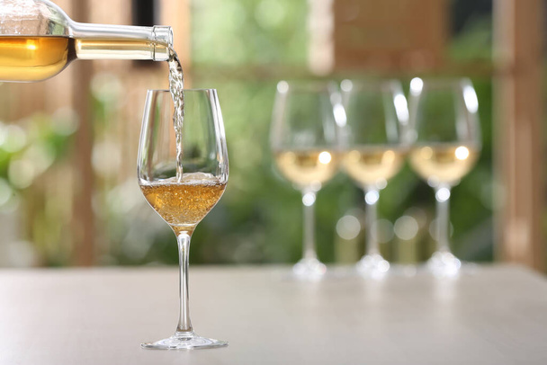 Pouring white wine from bottle into glass on table against blurred background, space for text - Fotó, kép