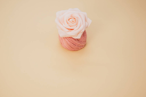 A top view of an artificial pink rose on a thread spool and pastel peach surface for a copy space - Foto, imagen