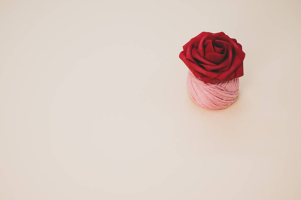 A closeup of an artificial red rose on a thread spool and pastel peach surface for a copy space - 写真・画像