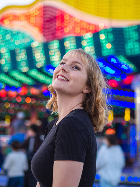 A vertical shot of a blonde woman with a piercing posing in an amusement park - Φωτογραφία, εικόνα