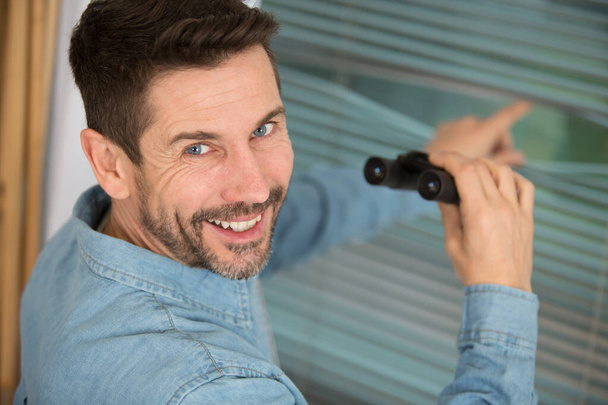 smiling man stood by window holding binoculars - Zdjęcie, obraz