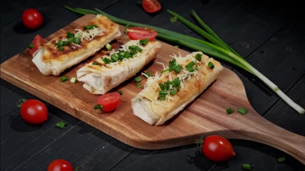Kawałki sera i szpinaku zawinięte tortille z grilla z zieloną cebulą i pomidorami na starej drewnianej desce. dania kuchni tureckiej - Materiał filmowy, wideo